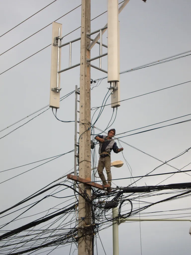 Tecnico su un palo della luce a Vientiane tra antenne cellulari e cavi della rete di telefonia mobile laotiana