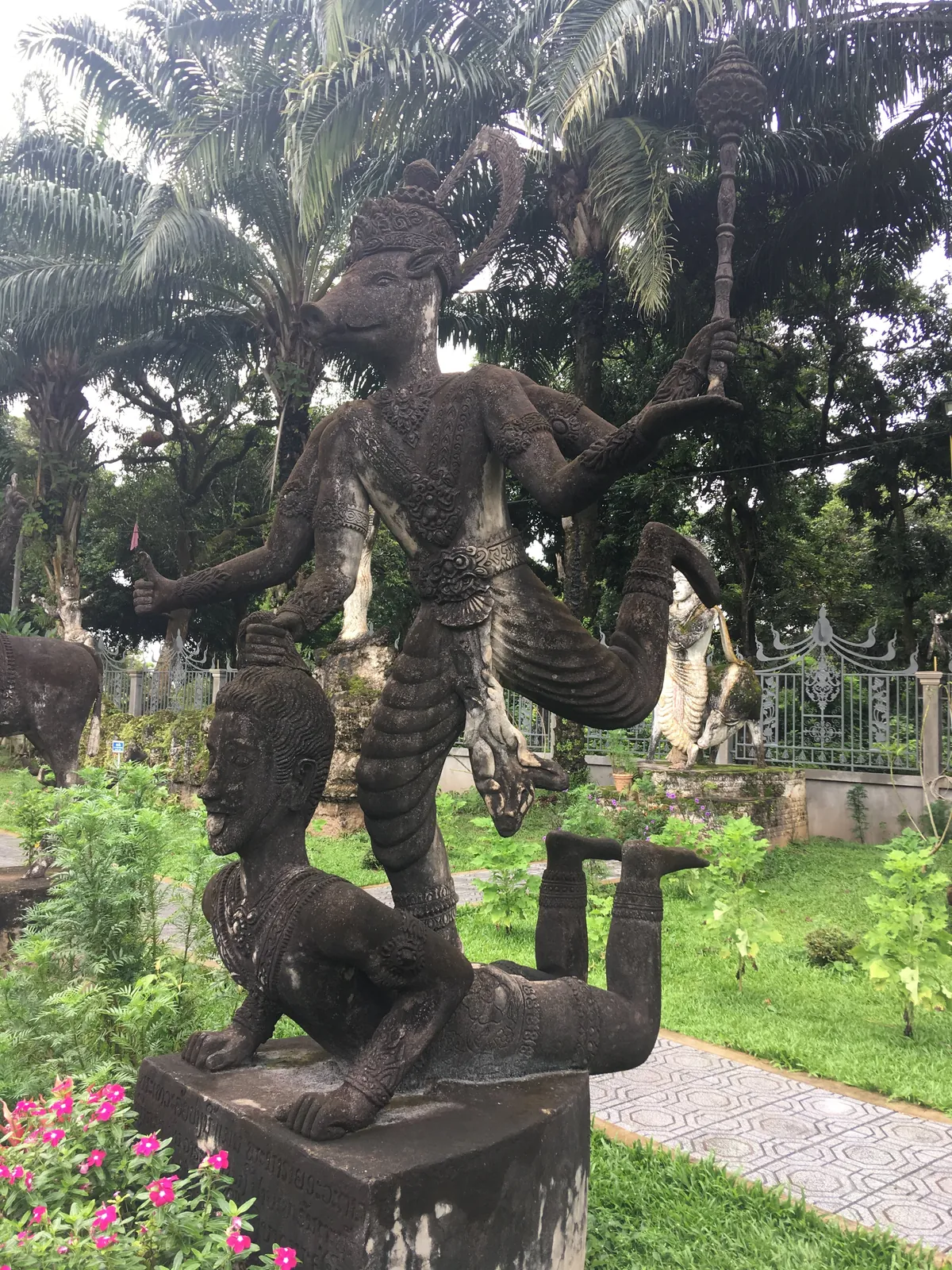 Statua del Buddha Park a Vientiane tra fiori rosa e vegetazione verde