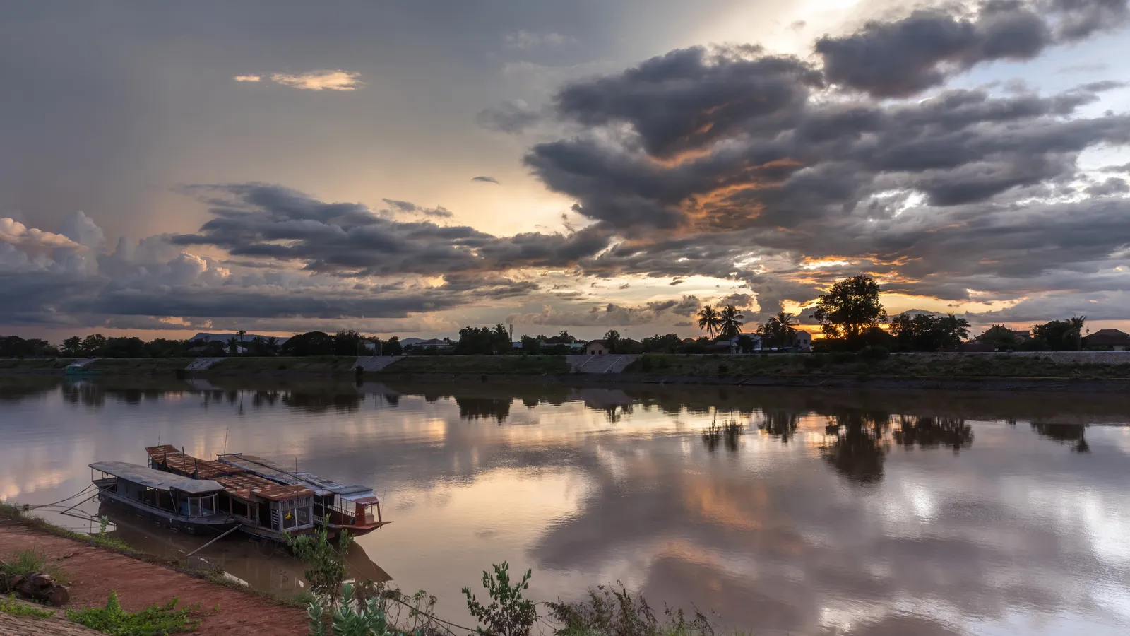 Tramonto sul fiume Xe Don a Pakse con barche ormeggiate e nuvole colorate riflesse nell'acqua