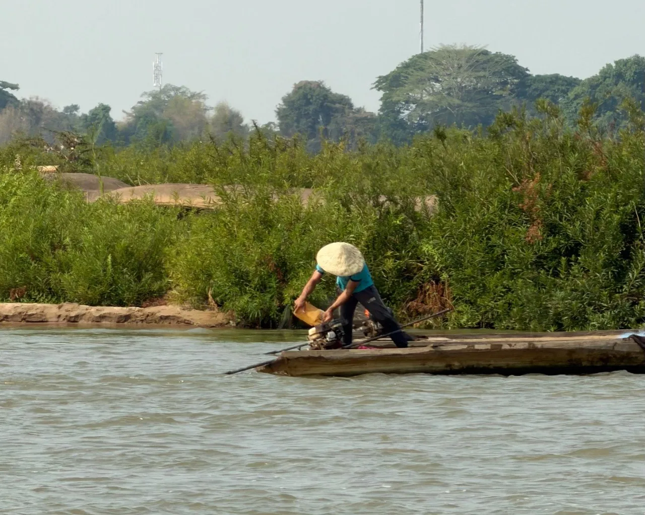 Pescatore con cappello conico su una barca di legno nel Mekong, Laos