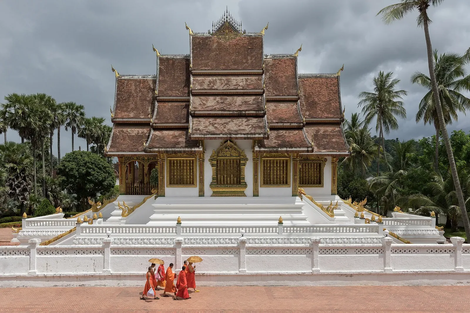 Monaci buddisti in abiti arancioni che camminano davanti al tempio Haw Pha Bang a Luang Prabang, in Laos