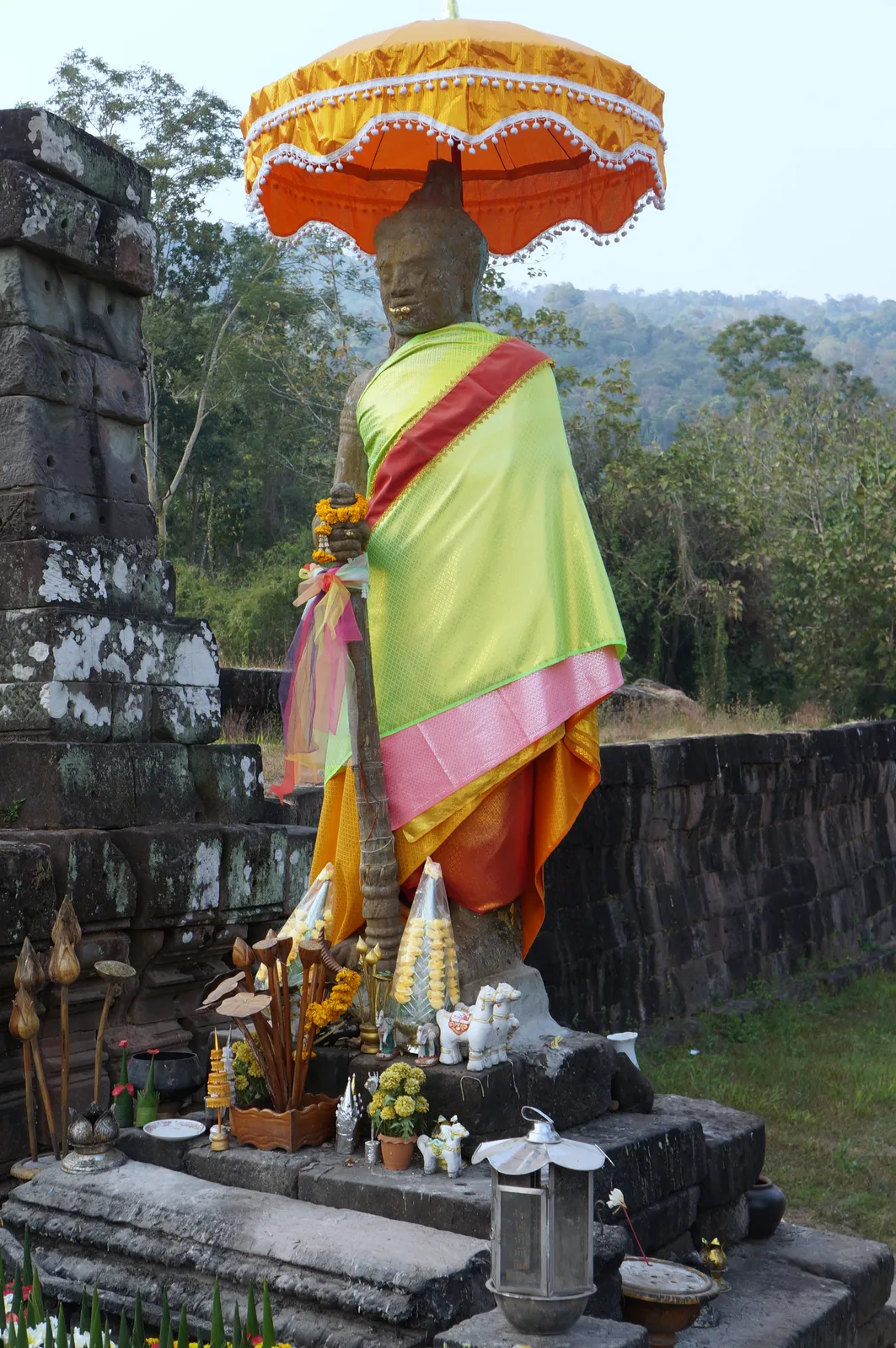 Le offerte floreali nel santuario di Wat Phou Statua adornata con stoffe colorate e ombrello cerimoniale nel tempio di montagna di Wat Phou, sito UNESCO di Champasak