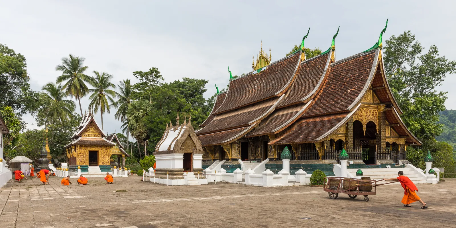 Monaci buddisti nel cortile del Wat Xieng Thong a Luang Prabang, tempio del XVI secolo con tetti a bassa falda e mosaici dorati